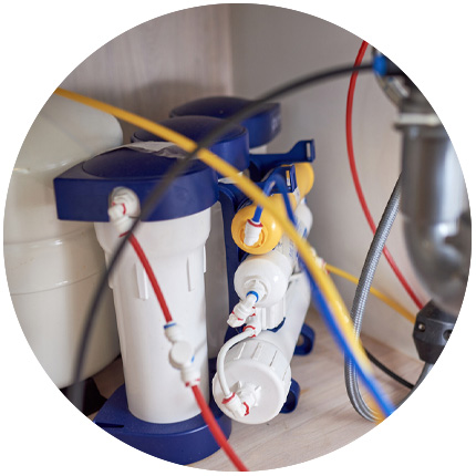 Under-sink reverse osmosis water filtration system with blue and white canisters connected by red, blue, and yellow tubing.
