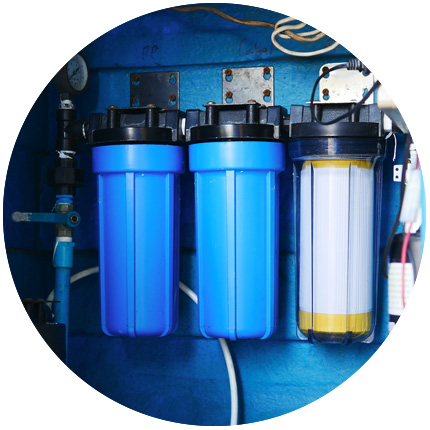 Three water filter canisters mounted on a blue background, with two blue canisters and one clear canister, part of a water purification system.