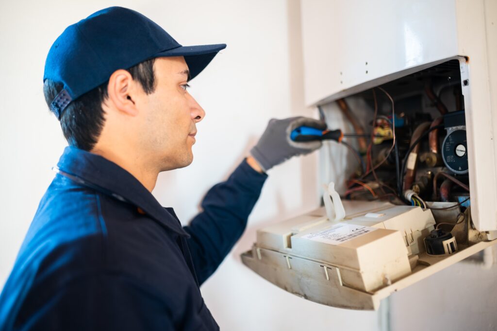 Technician repairing an HVAC unit, focused on electrical components with a screwdriver.
