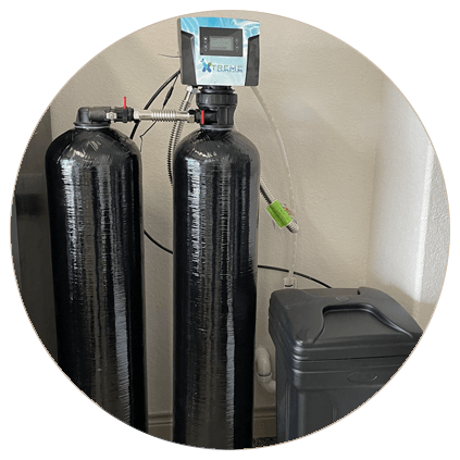 Home water softening system with dual black tanks and digital control valve, installed next to a trash bin.