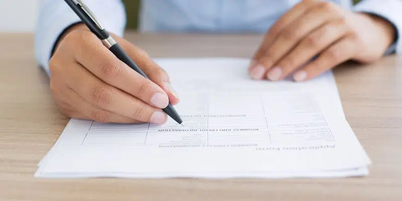 Person filling out an application form with pen