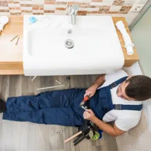 Plumber working under a bathroom sink.