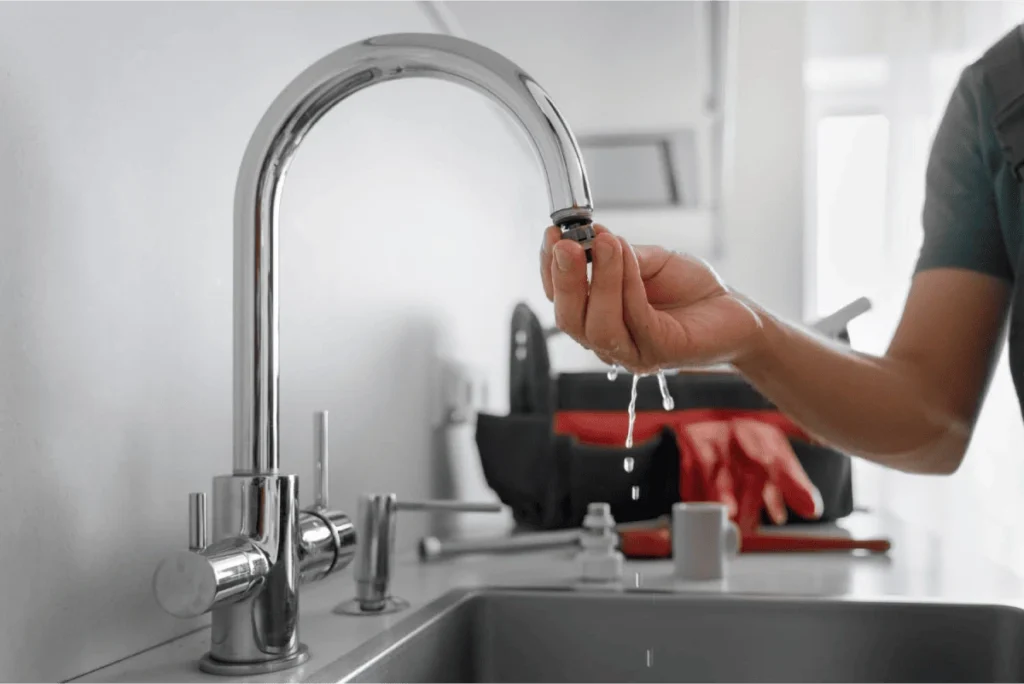 A person replacing an aerator on a kitchen faucet, with water dripping from the fixture.