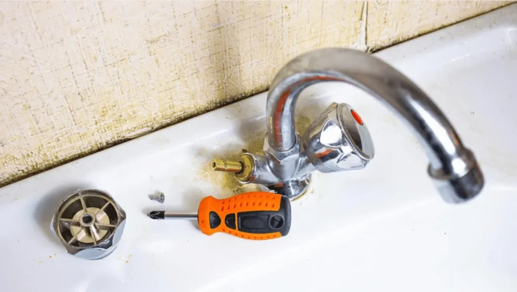 A disassembled sink faucet with a screwdriver and parts, showing a repair process.