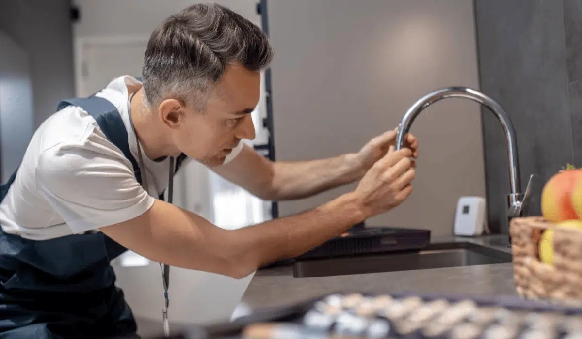 A plumber installing a new kitchen faucet with a focus on tightening the connections.