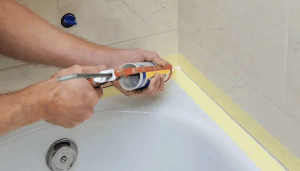 A person applying caulking sealant around the edge of a bathtub to ensure a waterproof finish.