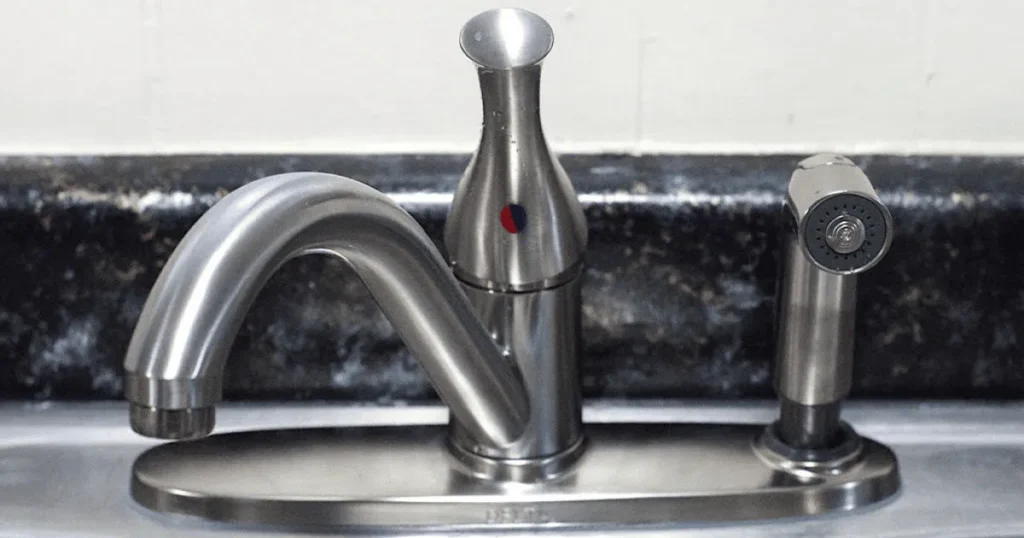 A stainless steel kitchen faucet with a hot and cold water indicator next to a matching side sprayer.