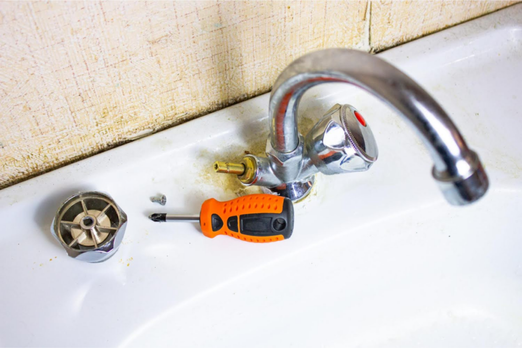 A disassembled sink faucet with a screwdriver and parts, showing a repair process.