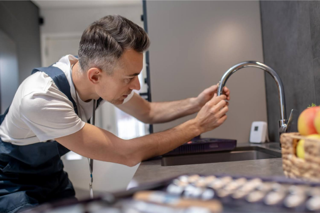 A plumber installing a new kitchen faucet with a focus on tightening the connections.