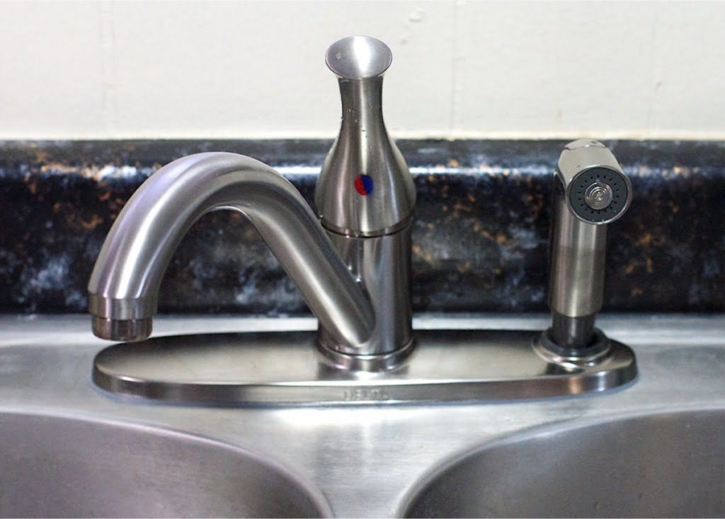 A stainless steel kitchen faucet with a hot and cold water indicator next to a matching side sprayer.