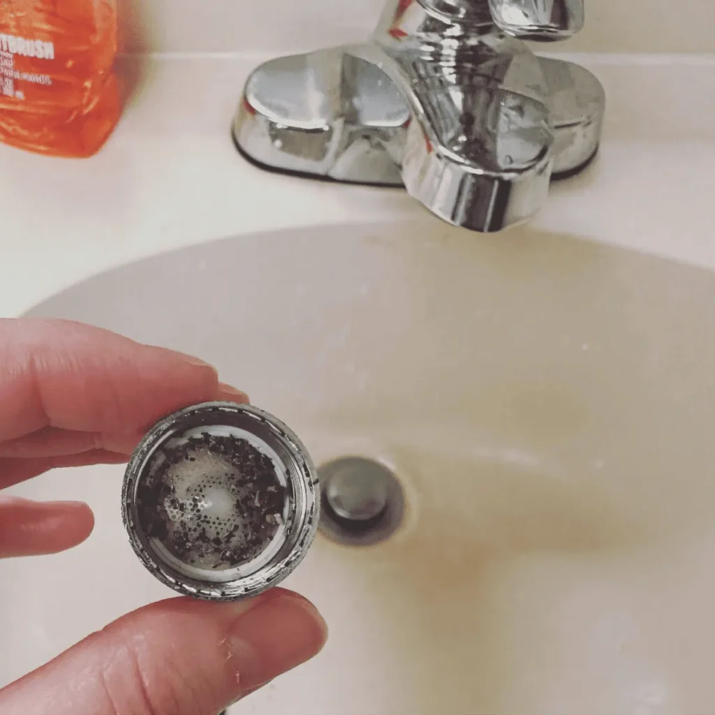 A hand holding a faucet aerator filled with sediment and mineral buildup, illustrating the impact of poor piping on water quality and the need for repiping services.