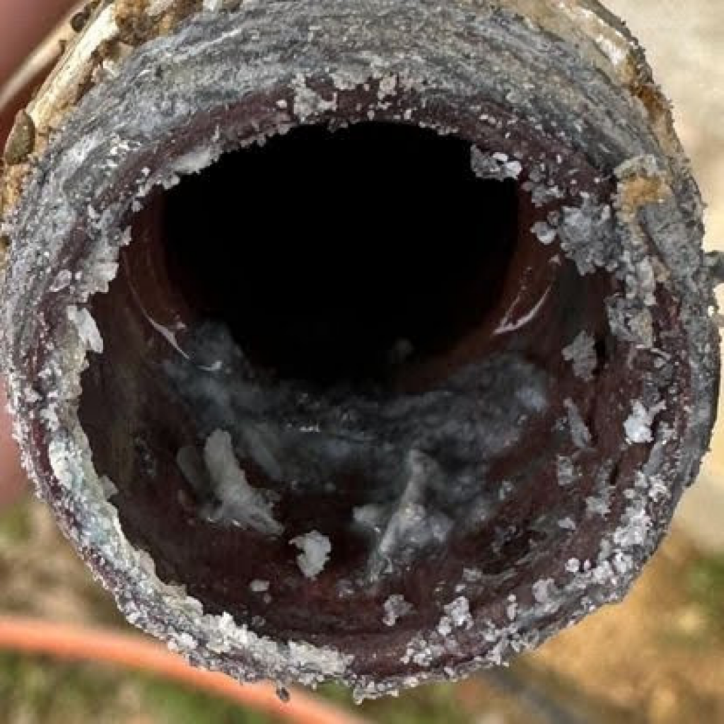 A close-up of a pipe severely clogged with mineral deposits and corrosion, showcasing the need for repiping to ensure clean water flow.