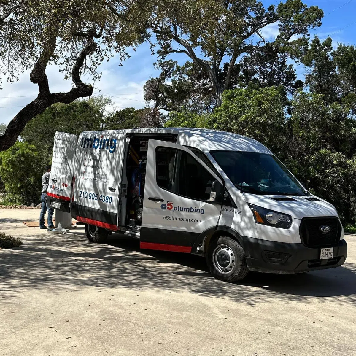 Yard Leak Detection in San Antonio 4 A plumbing service van with company branding parked on a driveway surrounded by trees.