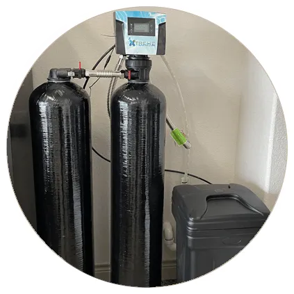 Home water softening system with dual black tanks and digital control valve, installed next to a trash bin.
