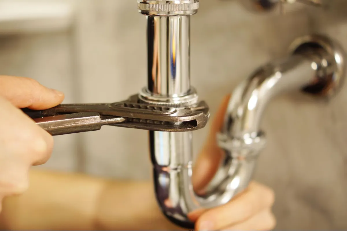 Close-up of hands using an adjustable wrench to tighten or repair a chrome plumbing fixture